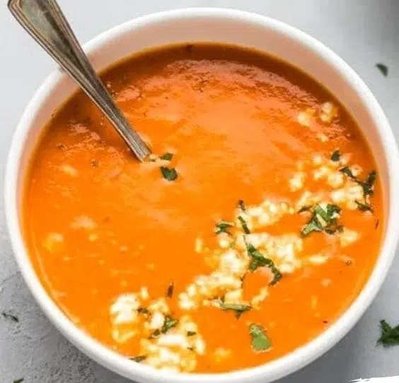 Bowl of easy tomato feta soup garnished with fresh herbs and feta cheese.
