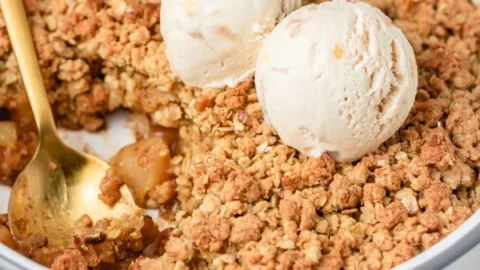 Bowl of simple apple crumble topped with ice cream on a wooden table