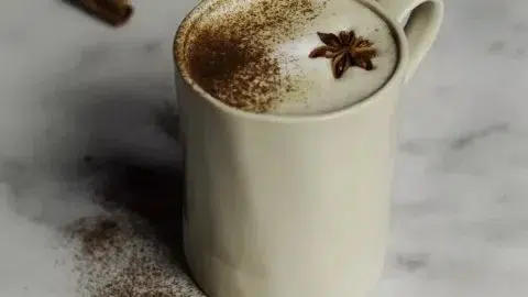 A steaming cup of spiced tea latte topped with frothy milk and spices