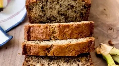 Sliced homemade banana bread on a wooden board with ripe bananas